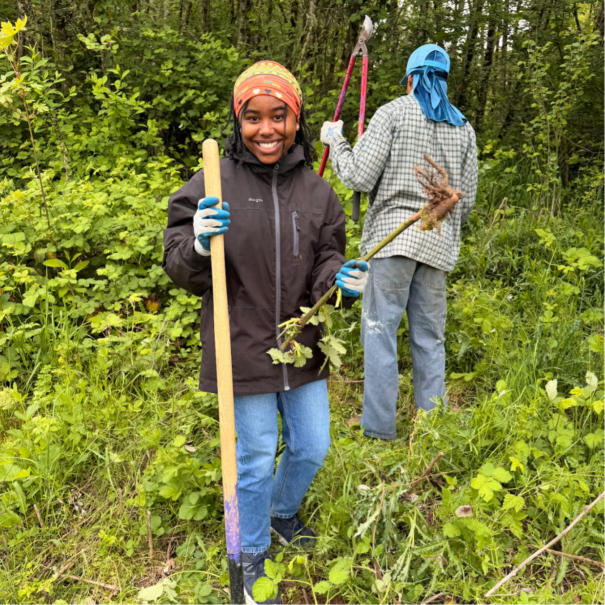 Grounding Waters student posing for a picture with.a smile, holding a shovel and plant root.