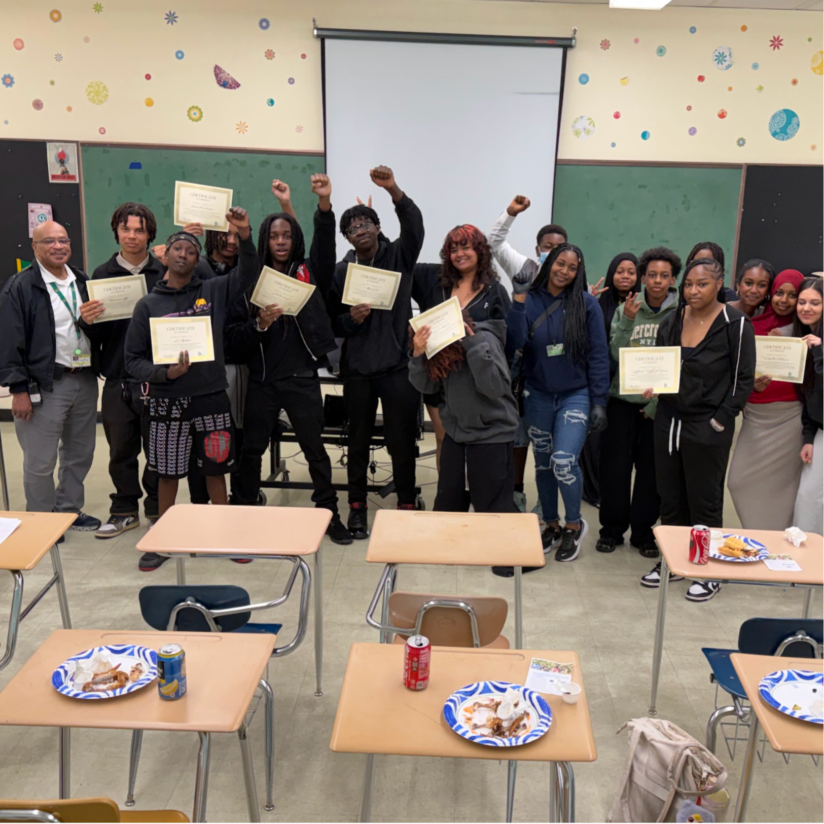 A group of Sowing Seeds students posing for a picture with their graduation certificates and their fists raised.