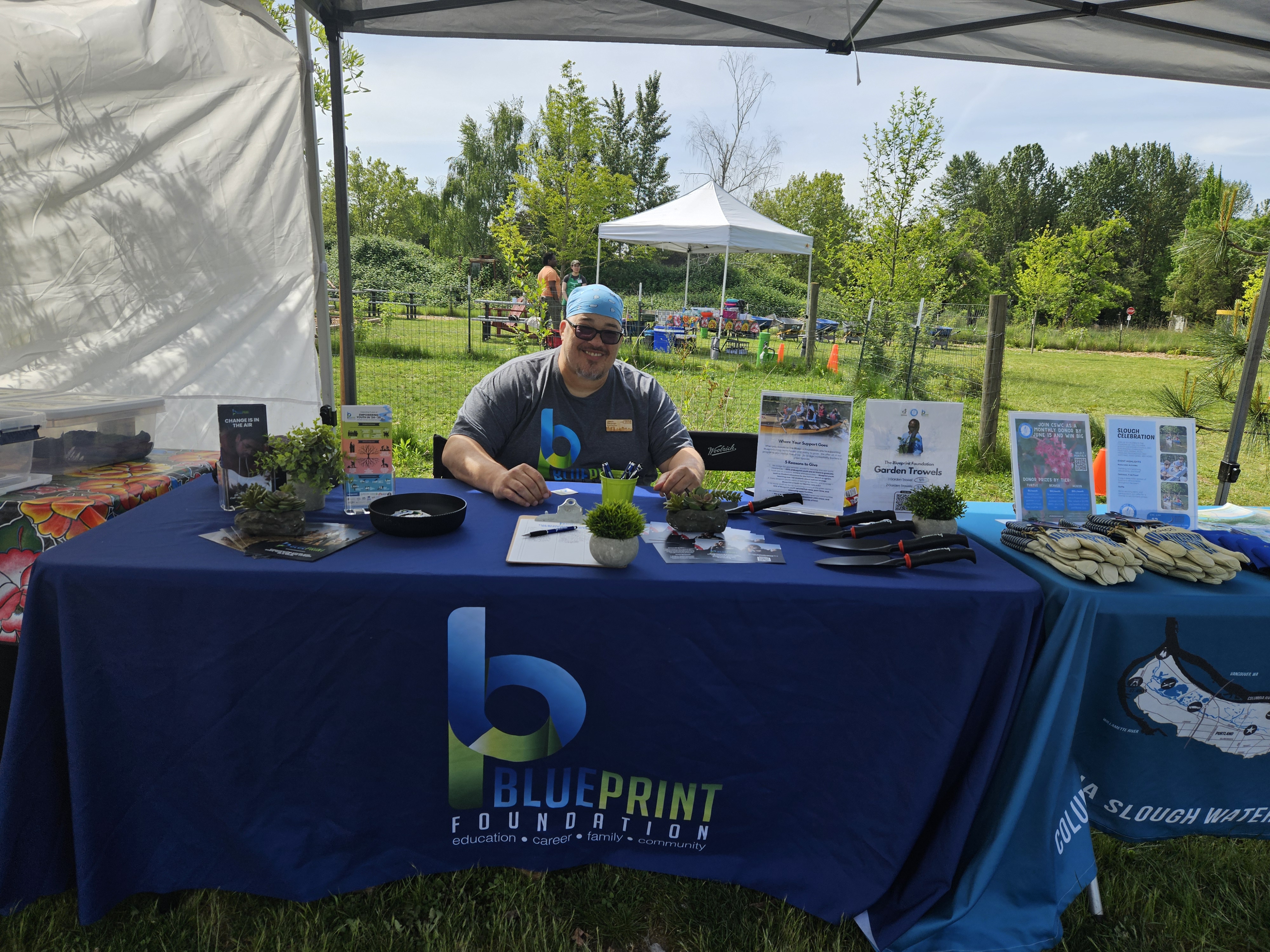Blueprint outreach table at Sparrowhawk Plant Sale with co-founder, Jason Stroman, sitting with a smile.