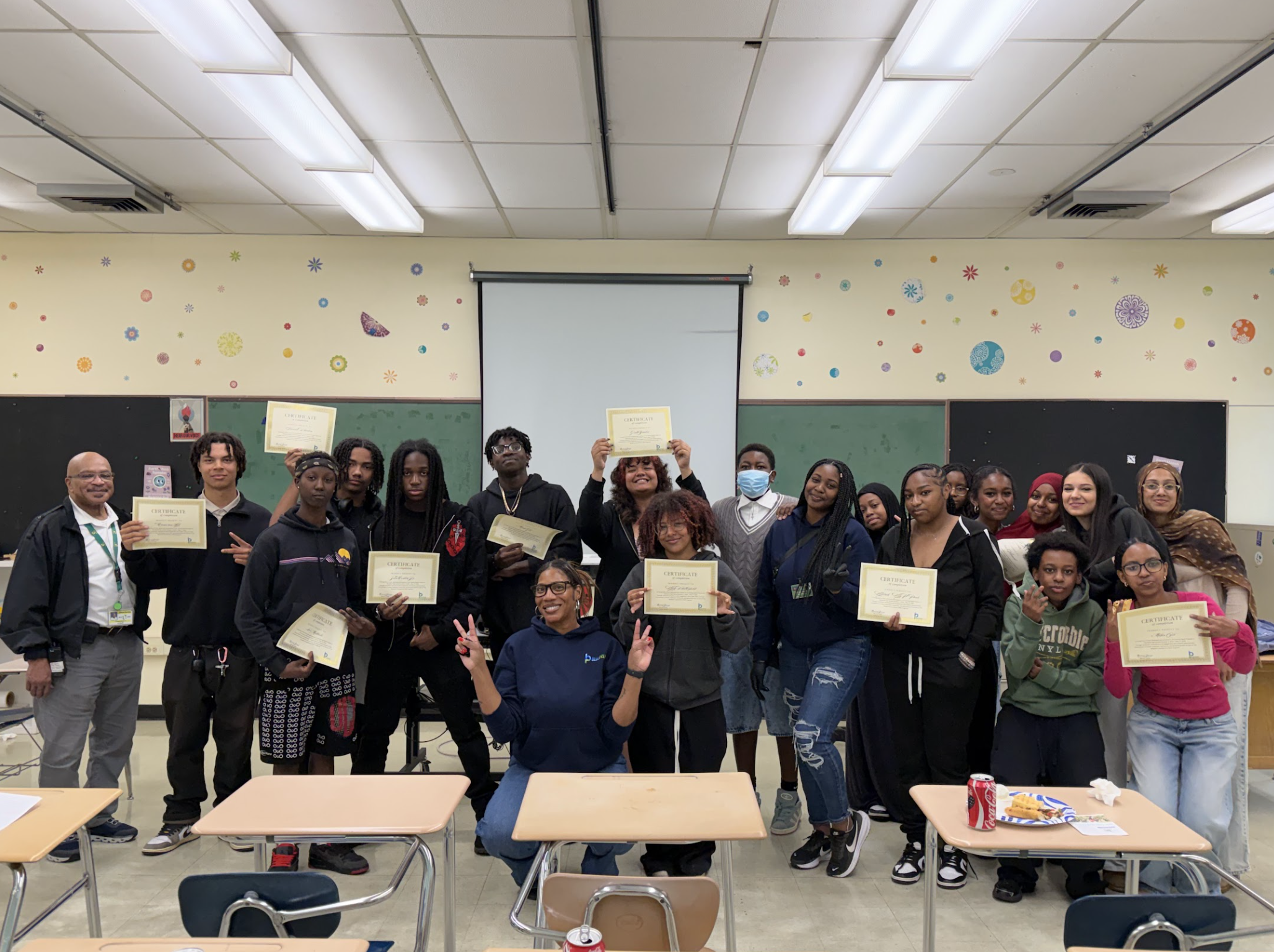 A large group of Sowing Seeds students & Blueprint staff huddled together for a picture. Everyone is smiling and holding graduation certificates.