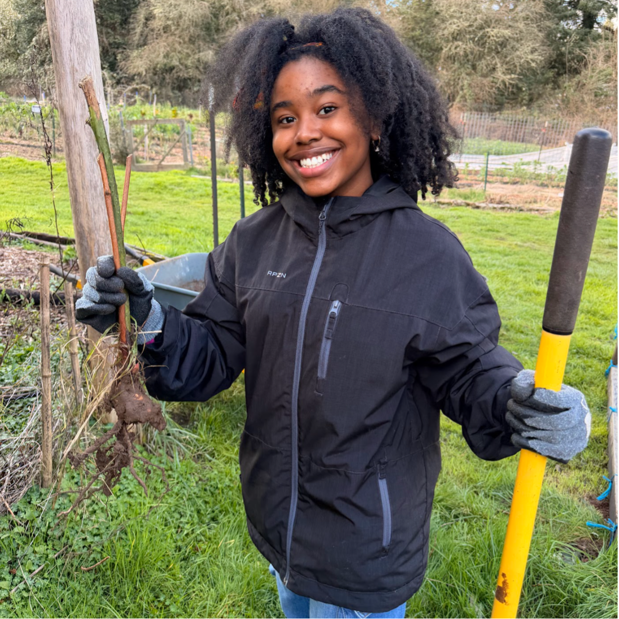 Blueprint student in a black rain jacket holding loppers and branches with a smile.