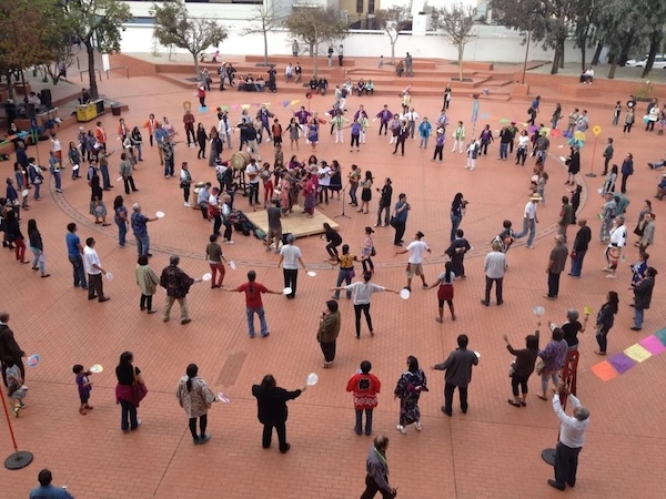 A photo of Great Leap’s FandangObon music and dance circle event. Many rings of attendees surround a group of musicians and dancers on a sprawling outdoor plaza.